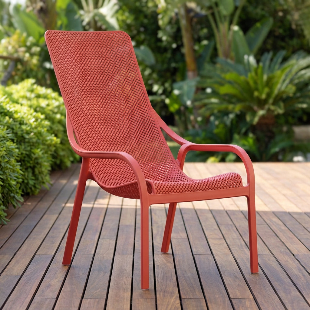 Create a high-resolution studio shot of the Net Lounge Chair, positioned centrally against a sleek, minimalist outdoor patio backdrop with lush greenery. Use softbox lighting to evenly illuminate the seat's enveloping, wave-like profile and textured, durab