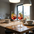 A lifestyle-inspired scene featuring the Zwiesel Sensa Flavoursome & Spicy (660ml) glasses on an upscale wooden dining table, captured with a 35mm wide-angle lens to create an inviting, warm atmosphere. The glasses are filled with a colorful, refreshing be