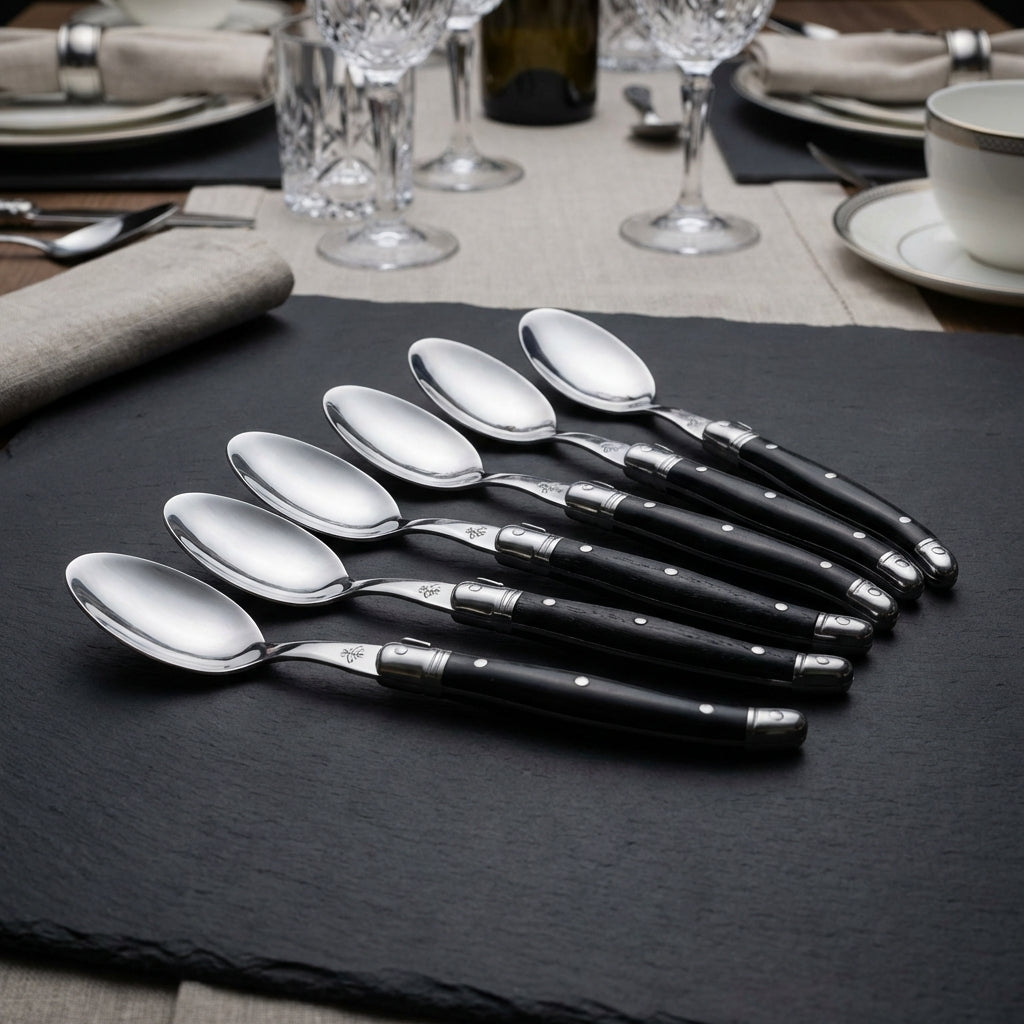 Capture a luxurious still life of the "Laguiole Spoons Black- Set 6" arranged elegantly on a dark matte surface in a high-end culinary setting. Use softbox studio lighting to highlight the sleek black handles with subtle reflections on the stainless steel 