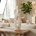 Depict the 'Standing Couple - White' sculpture in a chic home living environment, positioned on a rustic wooden console table. Use a natural, softbox light source from one side to mimic daylight, with additional fill light to soften shadows and bring out t