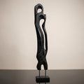 Capture a close-up of the 'Standing Abstract Wooden Art - Black' against a minimalist studio backdrop. Use a softbox lighting setup to highlight the rich textures and matte finish of the black wood, emphasizing the intricate handcrafted carvings. Set the c