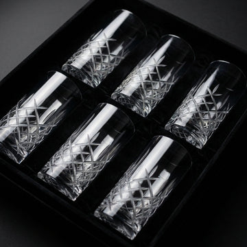 A sleek, high-resolution studio shot of the Stolzie New York High Ball 405ml glass arranged neatly in a custom-designed black velvet-lined box of six. The scene is illuminated with softbox lighting to emphasize the glass's clarity, smooth curves, and subtl