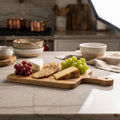 Capture a high-resolution image of the 'Serving Board Oak' in a luxurious, sophisticated kitchen setting. Use softbox lighting to create an even, warm glow that highlights the rich grain and natural texture of the American white oak. The camera is a Canon 