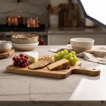 Capture a high-resolution image of the 'Serving Board Oak' in a luxurious, sophisticated kitchen setting. Use softbox lighting to create an even, warm glow that highlights the rich grain and natural texture of the American white oak. The camera is a Canon 