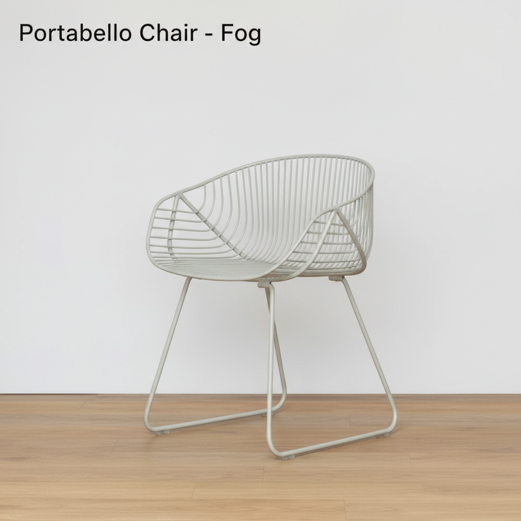 A lifestyle scene depicting the Portabello Chair - Fog in a stylish outdoor patio setting during daylight. The chair is styled as part of a cozy café setup with a rustic wooden table, potted plants, and ambient natural light filtered through surrounding fo