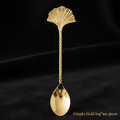 Create a luxurious product shot of the Gingko Gold leaf tea spoon, captured with a macro lens at 100mm focal length, emphasizing its intricate gold leaf detailing and exquisite craftsmanship. The scene is illuminated with softbox lighting to highlight the 