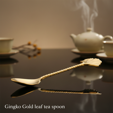 Visualize the Gingko Gold leaf tea spoon artistically arranged on a glossy, reflective surface, shot from a slightly elevated angle with a 50mm lens, capturing the shimmering gold and intricate leaf pattern vividly. Use HDR studio lighting to produce a bal