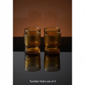 Create a high-resolution, studio-style image featuring the 'Tumbler Noho set of 4' arranged symmetrically on a sleek, reflective black glass surface. Use softbox lighting to craft a soft, ambient glow that highlights the rich amber hue and transparent clar