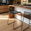 A luxurious lifestyle shot of the Dunedin Bar Stool in a chic modern kitchen setting with warm, natural lighting complemented by HDR studio lights to enhance the texture of the felted wool cushion and metallic wire frame. The camera is positioned at a slig