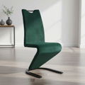 Create a high-end product shot of the Zed dining chairs in a sophisticated interior setting. Use softbox lighting to highlight the luxurious velvet texture of the deep emerald green fabric, capturing the subtle sheen and plush quality. The camera should be