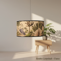 Create a high-resolution, studio shot of the 'Bamboo Lampshade - Cranes' hanging elegantly in a modern living room setting. Use a softbox lighting setup to highlight the intricate metal rims and vibrant printed images of lush leaves and tropical birds. Cap
