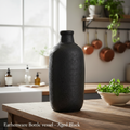 Generate a lifestyle scene showcasing the ‘Aged Black’ Earthenware Bottle vessel in an elegant, rustic kitchen setting. Position the vessel on a weathered wooden countertop illuminated by natural diffused daylight coming from a nearby window, creating a so