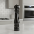 A highly detailed, studio-quality image of the 'Taylors Pepper Mill 25cm Black' set against a sleek, modern kitchen countertop. Illuminated by softbox lighting that creates gentle, even highlights on the smooth matte black surface of the pepper mill, empha