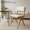 A sleek, contemporary dining room scene featuring the Cortez Dining Chair prominently positioned at a modern glass table. The chair, with its natural timber finish and removable cushions made from recycled plastic bottles, is illuminated with softbox light