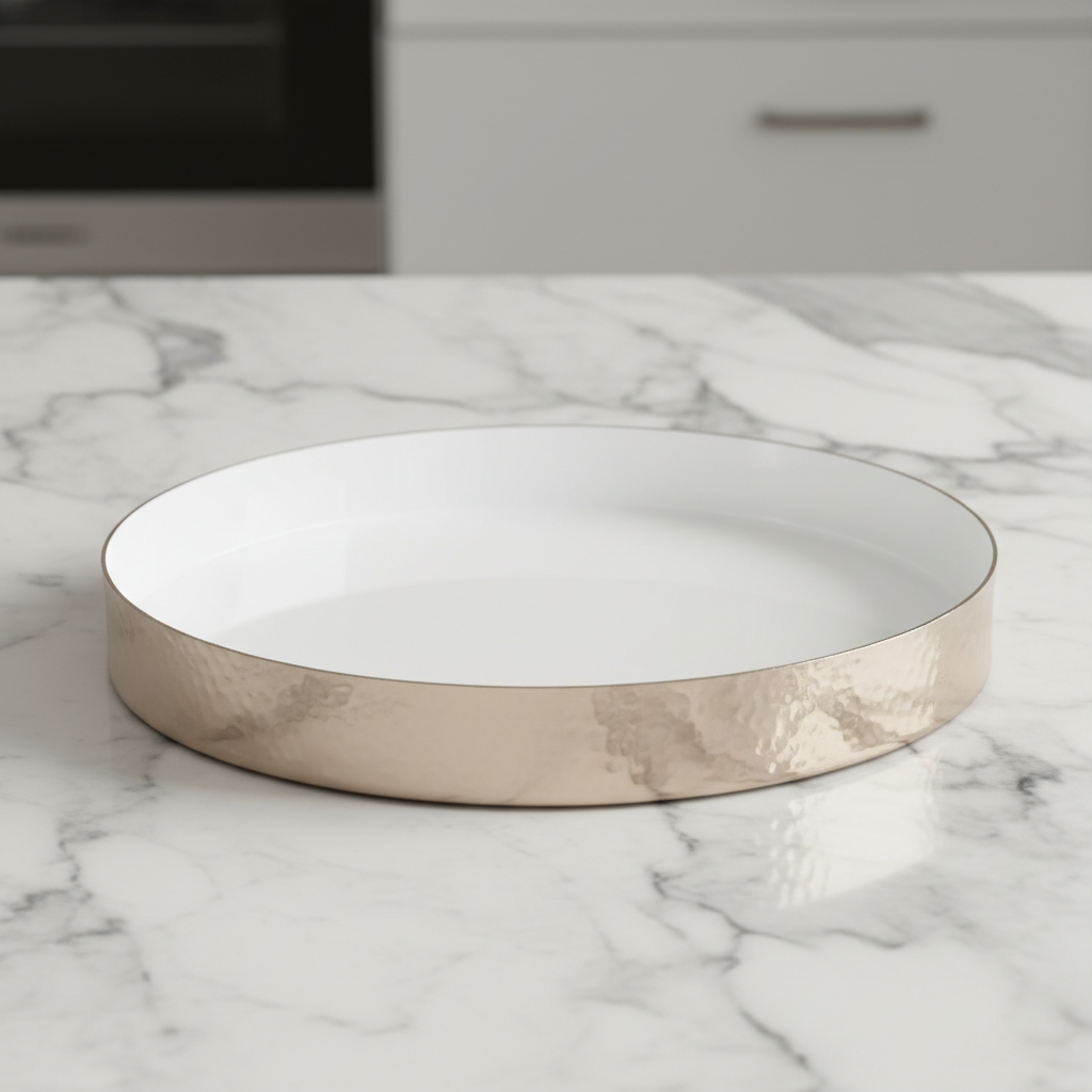 A highly detailed studio shot of the Hammered Round Tray -30cm, White enamel, placed on a sleek marble countertop under softbox lighting that emphasizes its glossy white finish and hammered texture. The camera uses a macro lens at 50mm, with a shallow dept