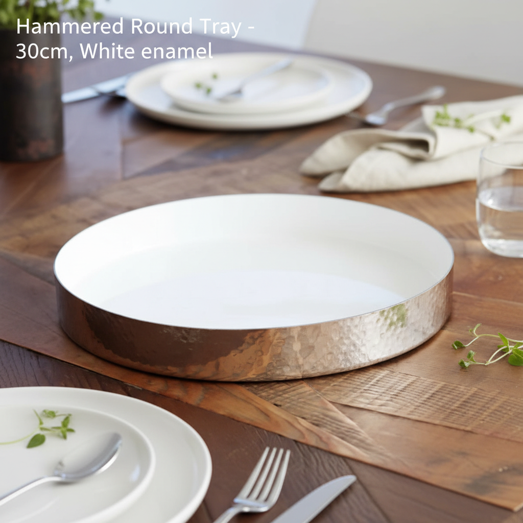 An elegant lifestyle setting featuring the Hammered Round Tray -30cm, White enamel on a rustic wooden dining table lit by HDR studio lighting that enhances its glossy finish and textured hammered surface. The shot is taken from a slight high angle with a 3