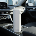 A lifestyle scene featuring the Frank Green Bottle 595ml Cloud in a stylish car interior. The shot is a wide-angle, overhead perspective, with the bottle placed snugly in a car cup holder, showcasing its perfect fit. The lighting is natural daylight filter