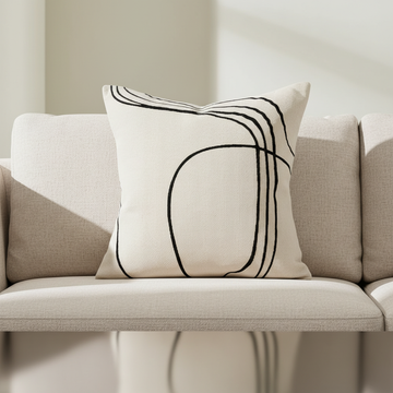A close-up, high-resolution image of the Loveline Ecru Cushion, shot with a professional DSLR camera using a 100mm macro lens to capture intricate embroidery details. The cushion is placed on a minimalist, modern sofa in a well-lit studio environment with 