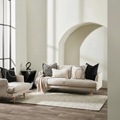 A styled lifestyle scene showcasing the Loveline Ecru Cushion elegantly resting on a contemporary armchair in a chic, well-decorated living room. The scene is lit with diffused daylight through large windows, creating a soft, natural glow that enhances the