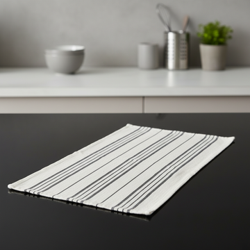 Capture a high-end product shot of the Tea Towel Black Linen from Winkler Karma, presented flat on a sleek, reflective black surface in a modern, minimalist kitchen setting. Use HDR studio lighting with softboxes to evenly illuminate the textured linen fab