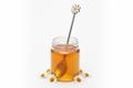 Jar of honey with a spoon and daisy-shaped handle on a white background